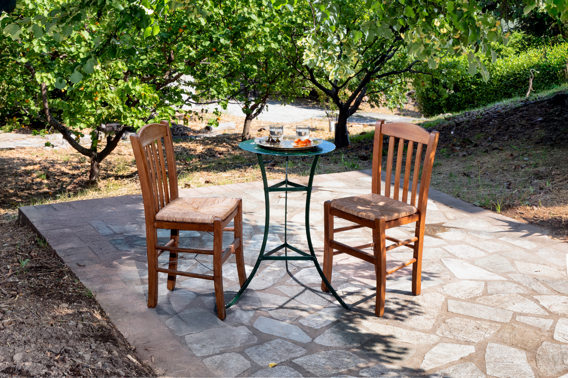 Two wooden chairs beside a small table under the trees at Villa Annelies